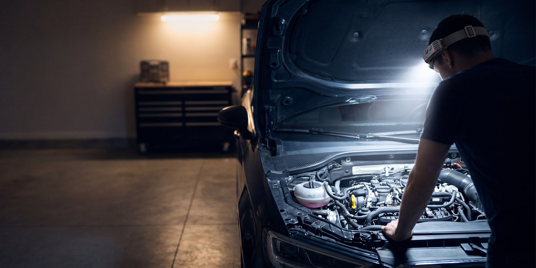 Headlamp in use under a car hood in a garage